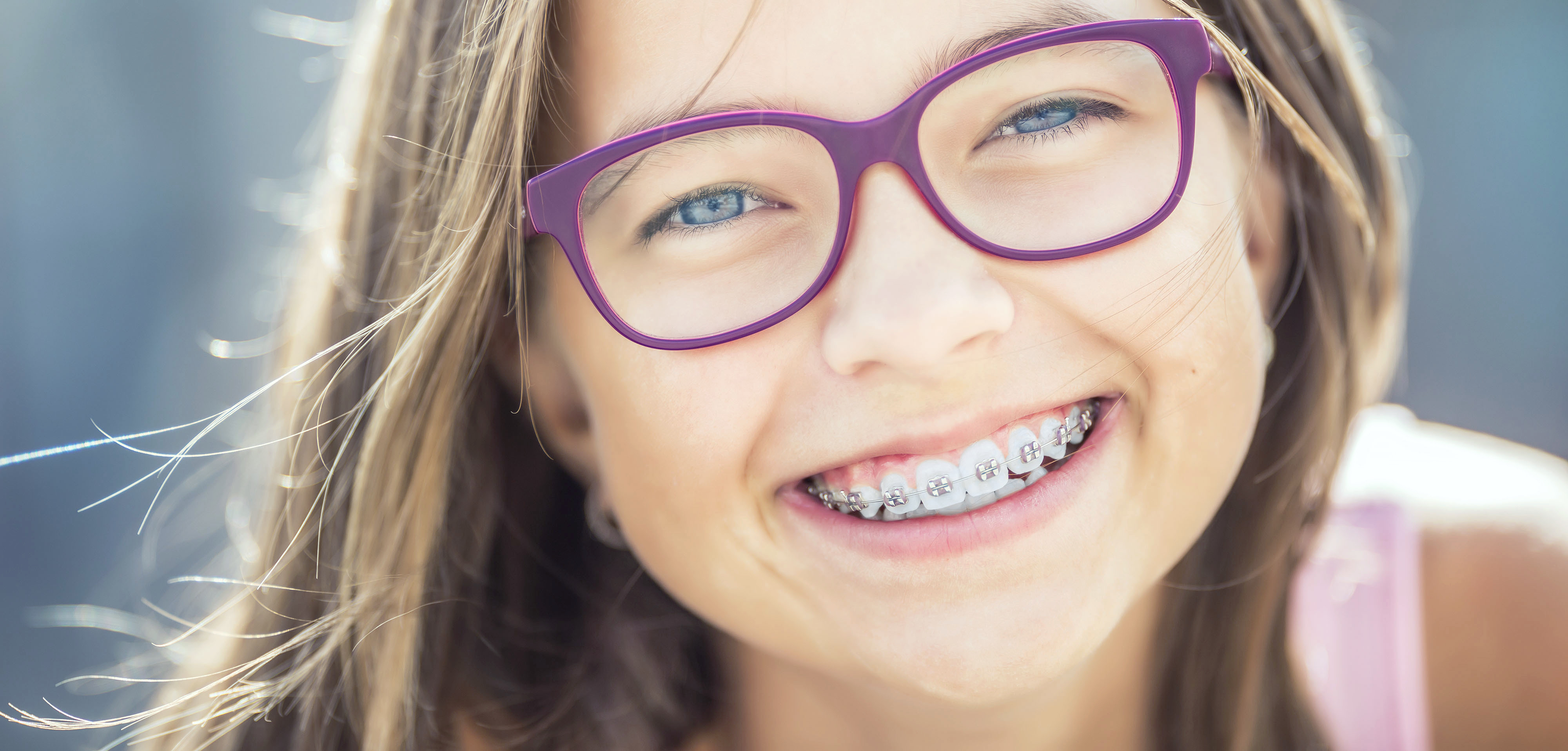 Eine lächelnde Person mit Zahnspange und violetter Brille – ein Bild, das die kieferorthopädische Behandlung als Teil des Leistungsspektrums einer modernen Zahnarztpraxis hervorhebt.