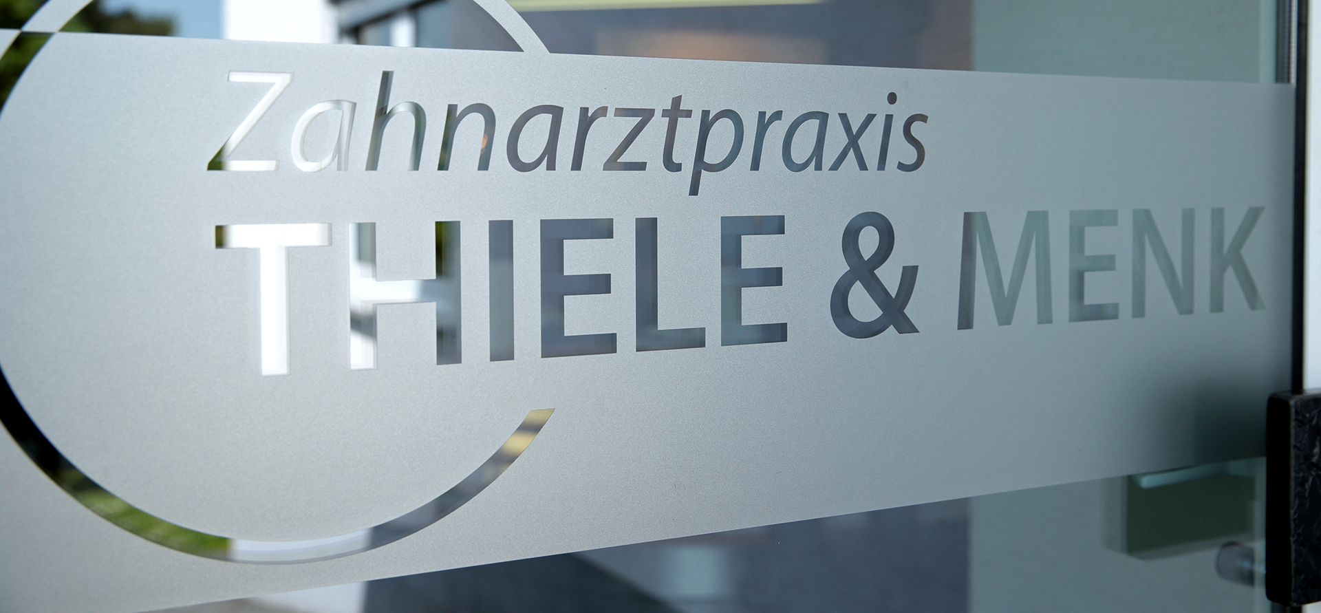 Türschild aus Milchglas mit der Aufschrift „Zahnarztpraxis Thiele & Menk“ – einer auf moderne Zahnheilkunde spezialisierten Praxis.