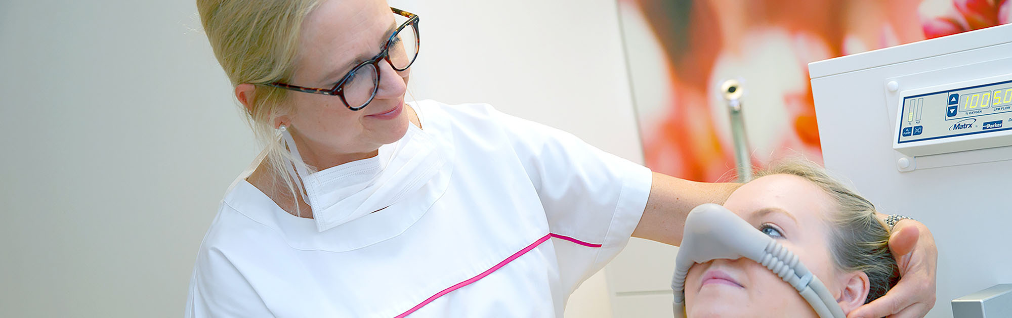 Eine Zahnärztin assistiert einer Patientin mit einem Nasenmasken-Gerät für Lachgassedierung in der modernen Zahnarztpraxis Thiele & Menk in Weilburg, die auf persönliche Beratung und umfassende zahnmedizinische Leistungen spezialisiert ist.
