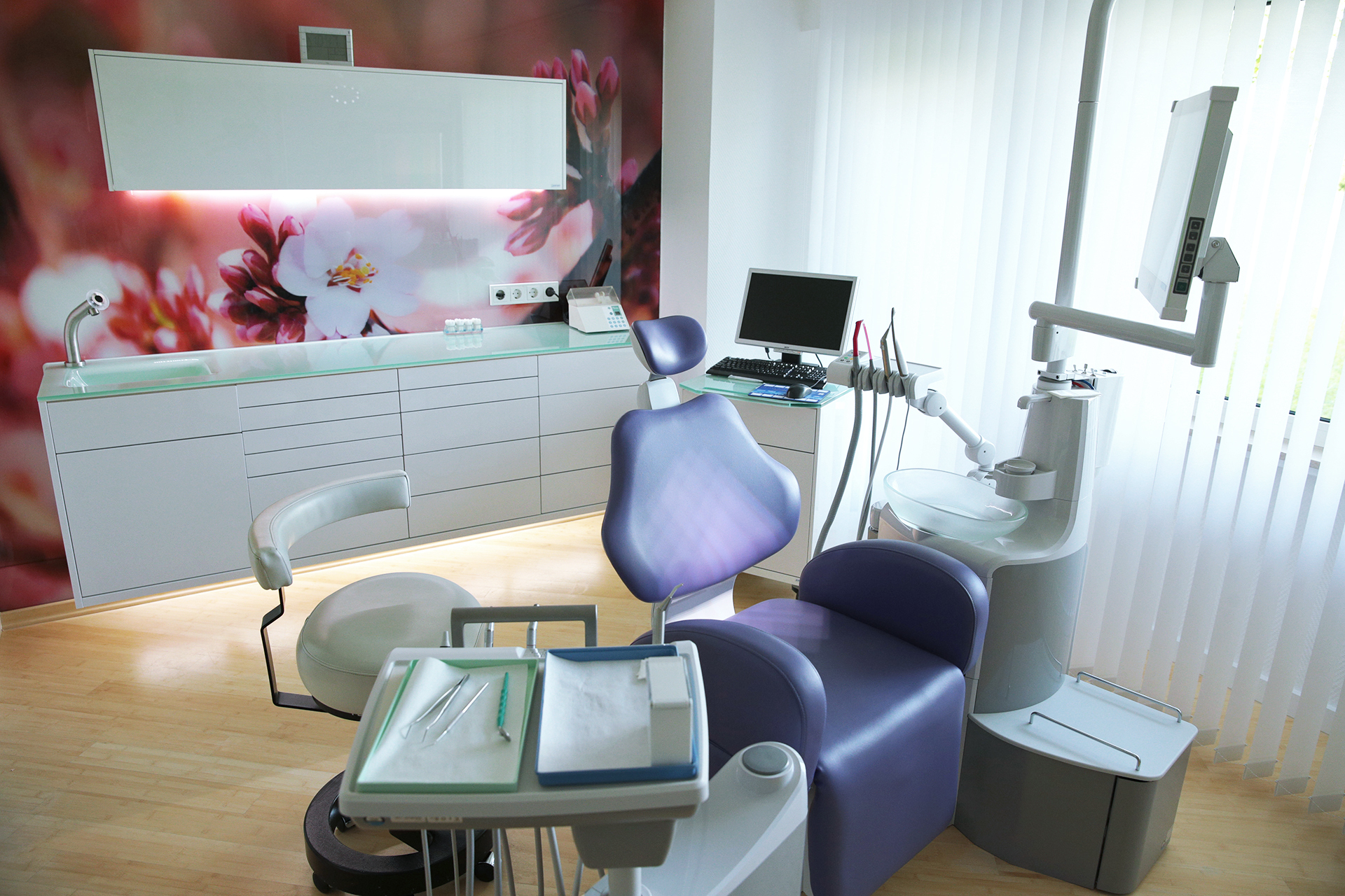 Modernes Zahnarztzimmer mit lila Behandlungsstuhl, digitalem Equipment und floraler Wanddekoration – repräsentiert die zeitgemäße Zahnmedizin der Praxis Thiele & Menk in Weilburg.