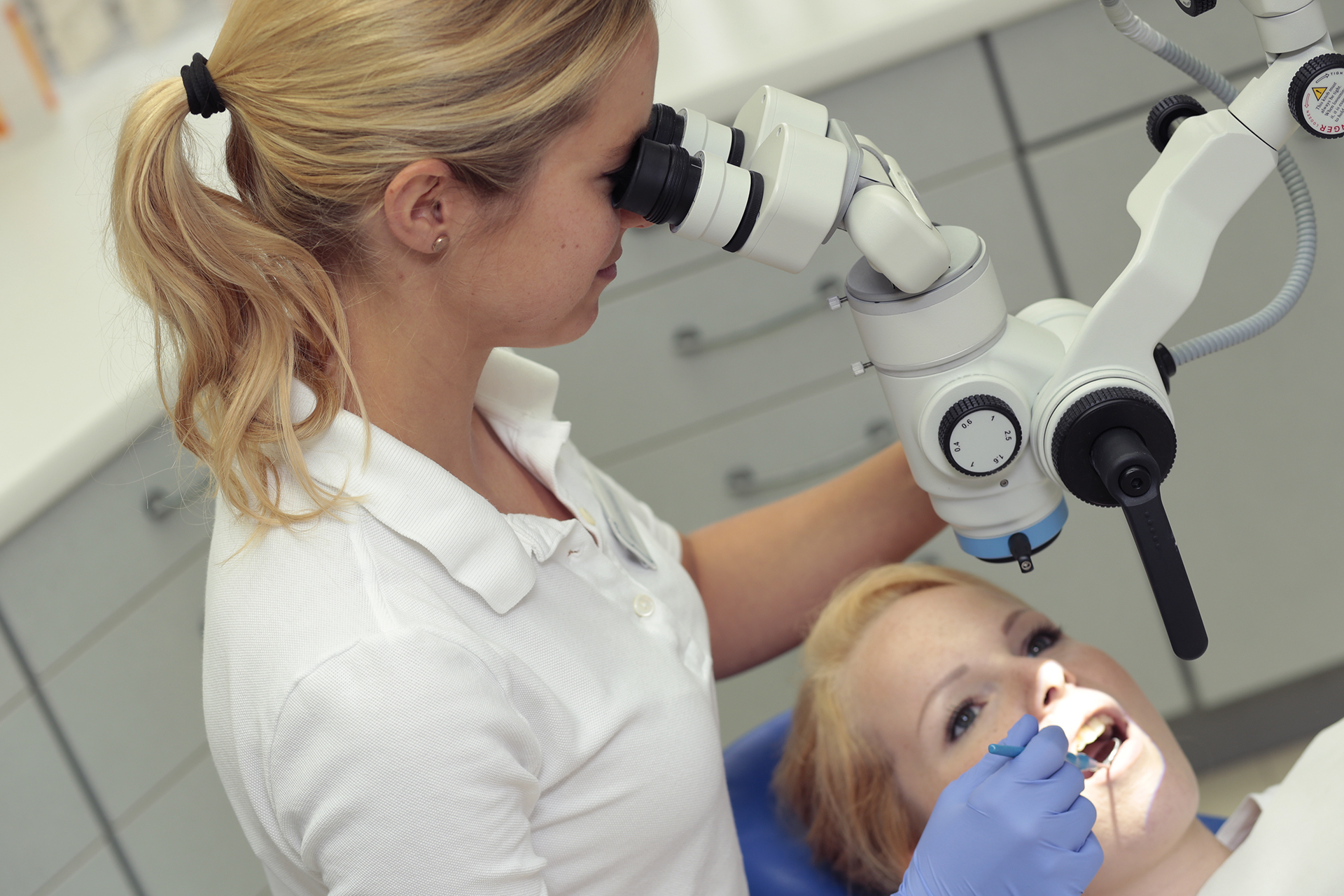 Eine Zahnärztin in weißer Uniform führt eine mikroskopische Behandlung bei einer Patientin in der Zahnarztpraxis Thiele & Menk in Weilburg durch, die moderne Zahnmedizin für Patienten jeden Alters anbietet.